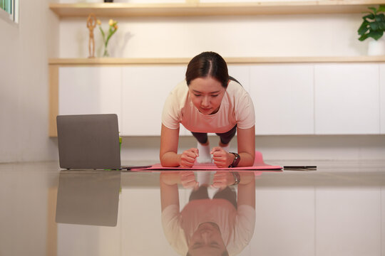 Asian woman doing plank core workout on mat with laptop tutorial for home fitness