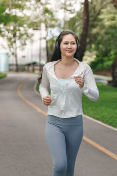 Asian woman jogging in park with headphones for outdoor cardio fitness workout