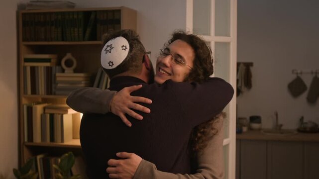 Caucasian adult man wearing kippah welcoming and hugging young adult brother arriving home for Hanukkah celebration. Footage suitable for Jewish holiday campaigns and family reunion commercials