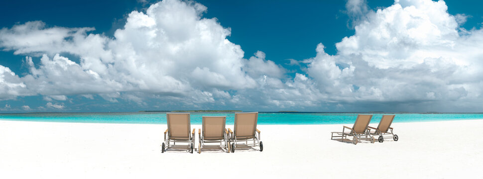 Panoramic view of empty sun loungers on white sand beach facing turquoise ocean under blue sky with fluffy clouds