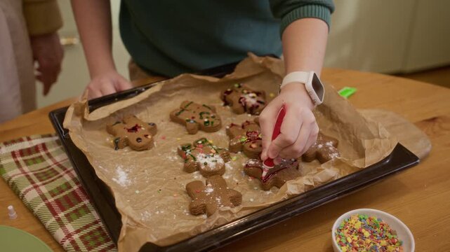 Caucasian child decorating gingerbread cookies with colored icing on baking tray from high angle. Footage suitable for Christmas baking commercials and holiday cooking campaigns