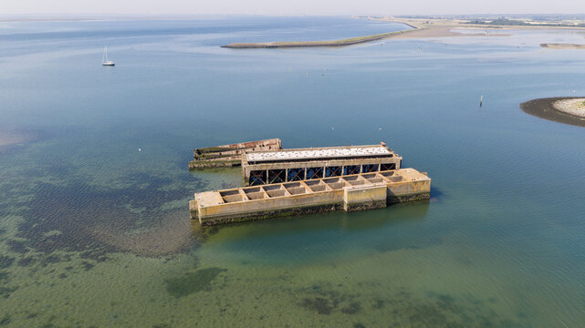 Aerial view of the historic concrete caissons at Inlaag Schelphoek, remnants of flood defenses, surrounded by the calm waters of the Oosterschelde in Serooskerke Schouwen, Zeeland, Netherlands.