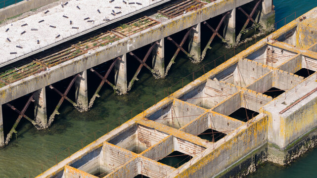 Aerial view of the historic Caissons Inlaag Schelphoek, featuring weathered concrete structures and steel reinforcement in the coastal waters of Serooskerke Schouwen, Zeeland, Netherlands.