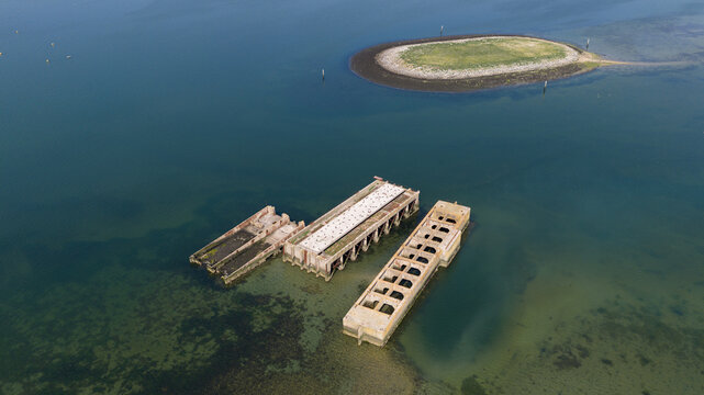 Aerial view of the historic concrete caissons at Inlaag Schelphoek surrounded by calm water and a small island in Serooskerke Schouwen, Zeeland, Netherlands.