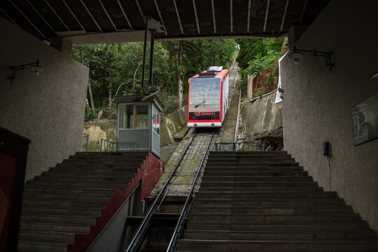 Tbilisi, Georgia - September 01, 2026: Red rail car climbs steep parallel tracks between broad stairways, concrete walls, and dense green vegetation at an inclined station
