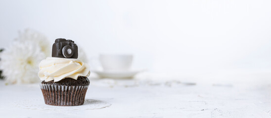 Cupcake decorated with a miniature chocolate camera, close-up with selective focus. Holiday greetings concept, banner with copy space for text © Nymphalyda