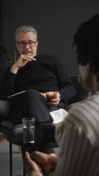 Vertical shot of middle aged Caucasian male psychotherapist gesturing and advising African American female patient. Clip suitable for mental health services and therapy marketing campaigns