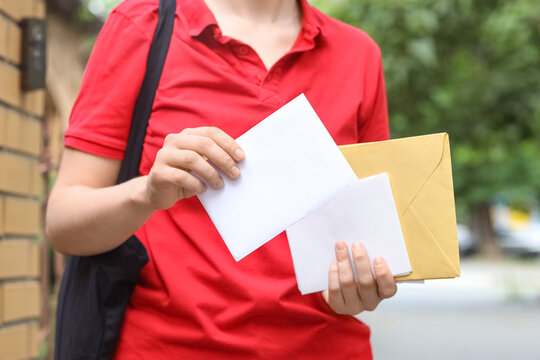 Mail delivery and logistics service, courier holding envelopes and packages for postal distribution in an urban neighborhood street setting