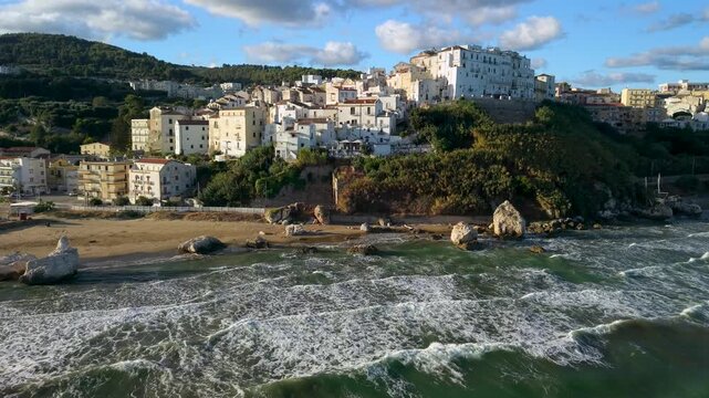 Rodi Garganico Puglia Italy 4k drone view of Scoglio del Leone rock at sunrise. Flyover of empty golden beach, old town on cliff and marina in Gargano, authentic untouched coast sea waves sounds