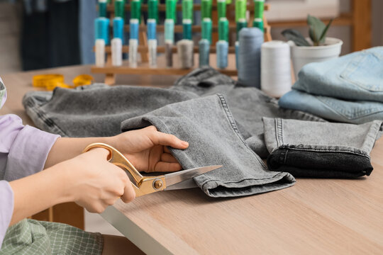Sustainable fashion and clothing repair, person cutting denim jeans with scissors for upcycling and tailoring in a sewing workshop