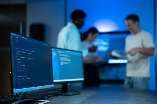 Computer screens displaying programming code in the foreground with a team of software developers collaborating in the background