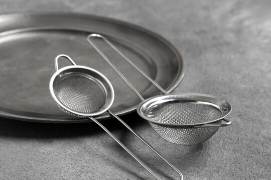 Culinary preparation and kitchen tools, stainless steel tea strainers and metal tray for cooking and baking tasks on a textured grey surface