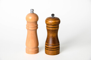 Two elegant wooden pepper mills side by side: light beige and dark walnut finishes with metal grinding tops on white background © kei u