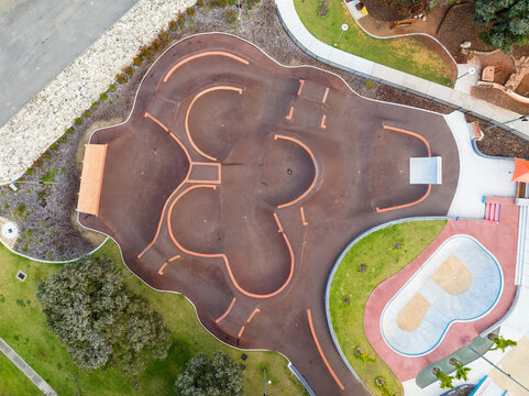 Aerial view of Duncraig Adventure Hub featuring a winding asphalt pump track with orange edges, a concrete bowl, and surrounding green parkland in Duncraig, Western Australia, Australia.