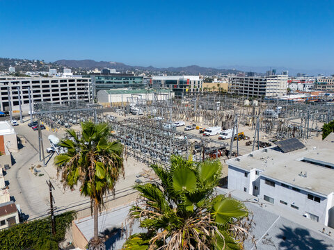 Aerial view of an electrical substation with transformers and power lines, with palm trees in the foreground and city buildings in the background in Los Angeles, California, United States.