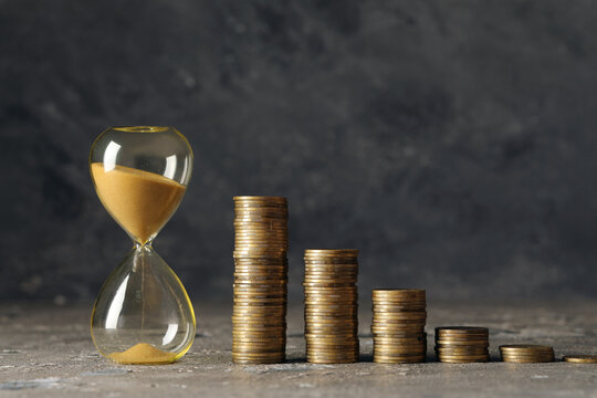 Time is money concept hourglass with falling sand and decreasing stacks of gold coins financial loss investment risk and economic decline