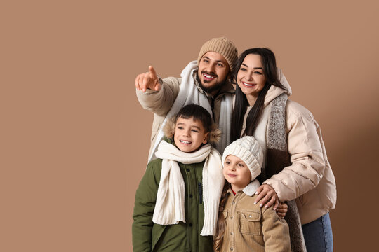 Family bonding and winter travel, happy parents with children pointing at something in warm winter clothing on a solid brown background