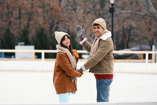 Winter leisure and romantic date, happy young couple ice skating together outdoors in park during cold season with warm winter clothing and joyful mood