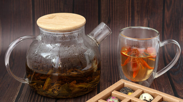 Spa relaxation and wellness concept. Close up of premium handcrafted blooming tea blossom in double walled glass cup near clear teapot in home office.