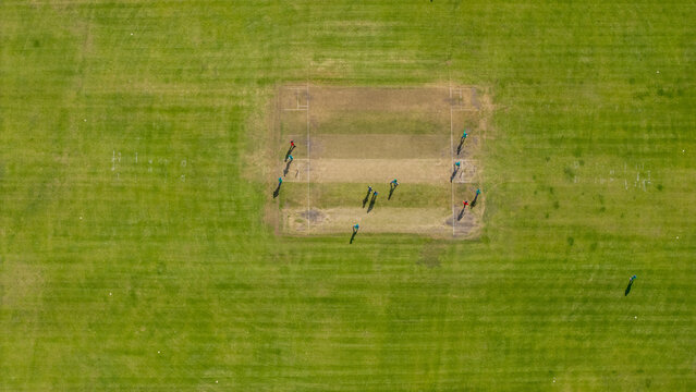 Aerial view of a cricket match being played on a green pitch with players positioned across the field in Oudtshoorn, Western Cape, South Africa.