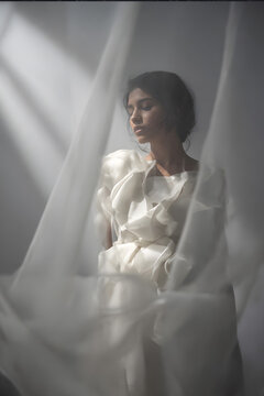 Fashion portrait with draped white fabric against dark moody background