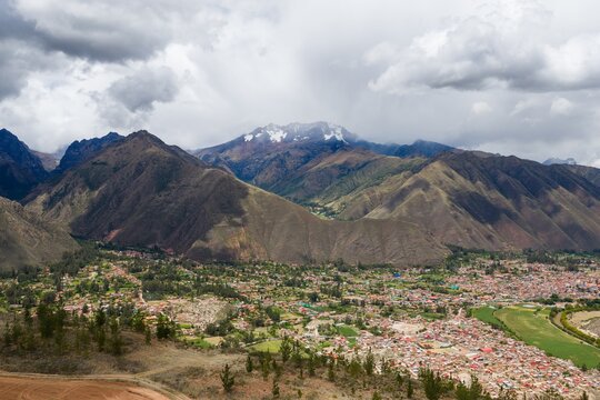 Aerial view of the historic town of Ollantaytambo in the Sacred Valley, surrounded by dramatic Andean mountains and lush green fields in Ollantaytambo, Cusco, Peru.