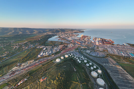 Aerial view of the Sermin industrial area featuring large storage tanks, the busy port of Koper, and surrounding agricultural fields in Koper, Koper, Slovenia.