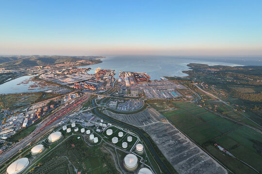 Aerial view of the Sermin industrial area and the Port of Koper, featuring large storage tanks, cargo terminals, and the coastline of the Adriatic Sea in Koper, Koper, Slovenia.