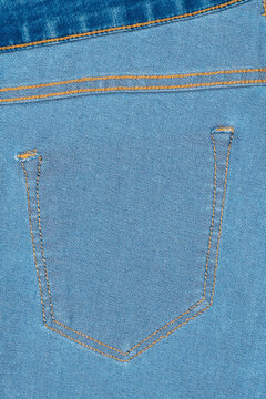 Detail shot of classic denim pocket with contrasting orange stitching on light blue jeans fabric. Textured weave clean lines emphasize craftsmanship. Ideal for fashion, retail, textile design use