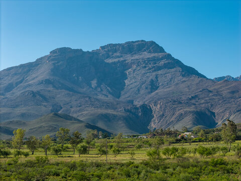 Aerial view of Swartberg Mountains with Towerkop peak overlooking fertile farmlands with crops and trees near Ladismith, Western Cape, South Africa.