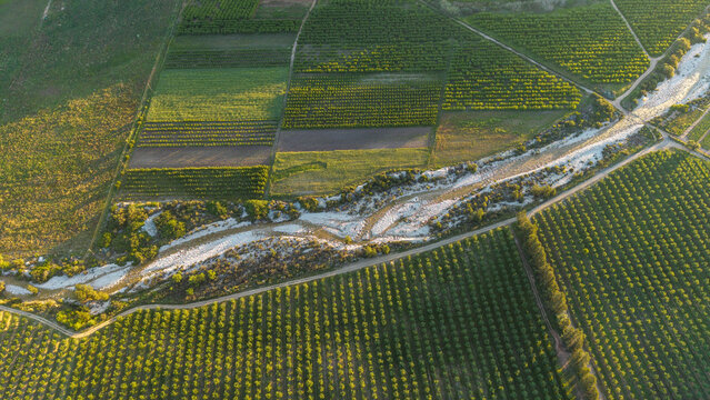 Aerial view of Klein Karoo farmlands with orchards and fields near Towerkop Mountain, showcasing vibrant agricultural patterns and a winding riverbed in Hoeko, Western Cape, South Africa.