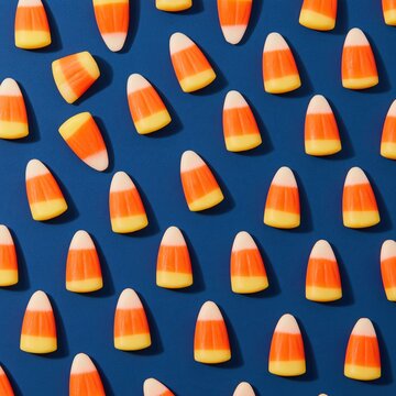 Candy corn pieces arranged in a precise grid pattern on a deep teal surface, featuring vibrant waxy colors for autumn and seasonal decor