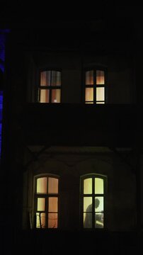 The silhouette in the glowing window of the house in the evening. A man is playing the piano