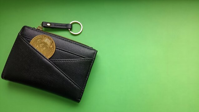 Gold bitcoin crypto coin peeking out of black leather wallet on green background with copy space, cryptocurrency storage concept. Wallet with money.