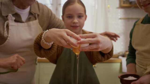 Caucasian girl cracking raw egg in slow motion while senior woman and boy watch during home culinary masterclass. Footage fits family cooking tutorials and food advertising