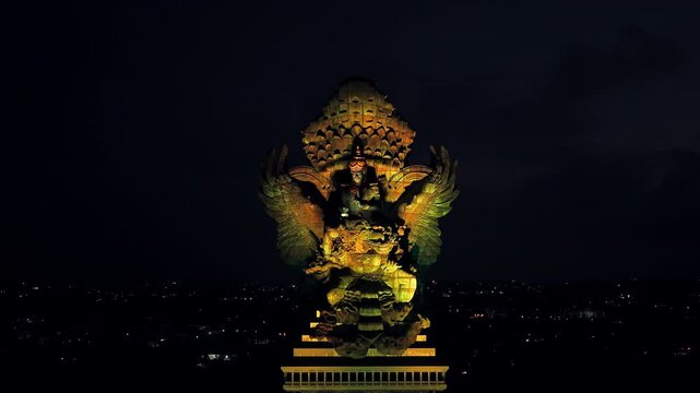 Garuda Wisnu Kencana statue at night dominates the dark Bali skyline with illuminated Hindu sculpture detailed craftsmanship and a striking cultural landmark rising aerial drone footage