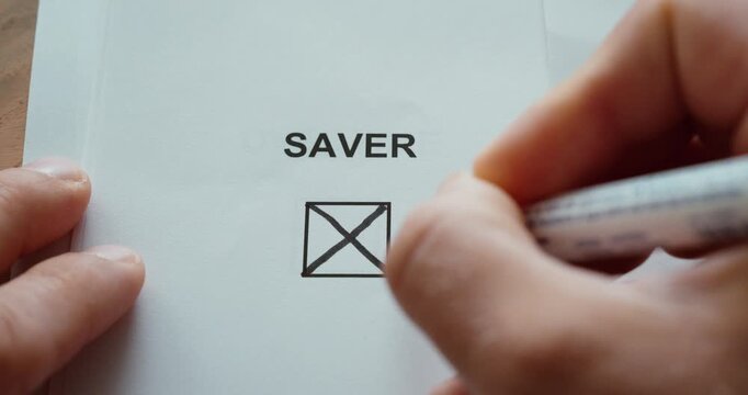 Close-up of a person using a black marker to check a checkbox labeled Saver on a printed paper. Concept of saving money, personal finance, budgeting, financial planning and responsible spending.