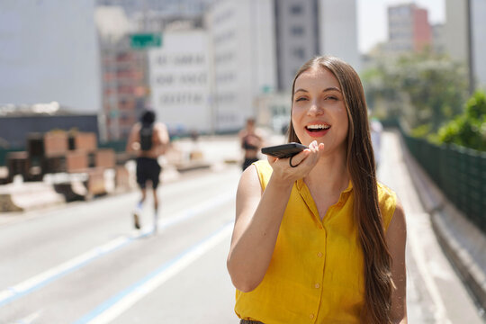 Smiling woman recording voice message on smartphone in Sao Paulo city street, Brazil