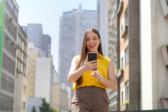 Business woman using smartphone app in Sao Paulo city street, Brazil. Low angle.