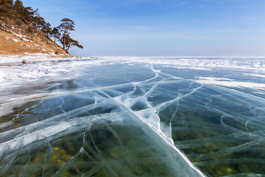 Beautiful winter landscape of frozen Lake Baikal. Thick, clear ice near shore on sunny February day. Coastal hills covered with coniferous forest within nature park. Winter walks, travel, recreation