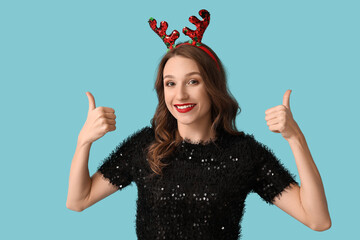 Young woman in reindeer horns showing thumb-up gesture on blue background © Pixel-Shot