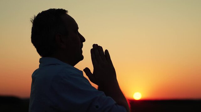 Faith in God. Human religion. Christian man praying dawn, close-up. Man confessing. Man praying with family, children, sky sun. Relaxation, meditation, nature. Asking for forgiveness. Hope. Silhouette