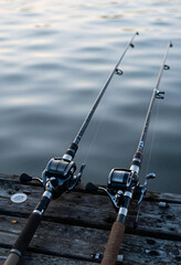 Fototapeta premium Leisure and recreation, two fishing rods with baitcasting reels resting on a wooden pier overlooking calm water for outdoor hobby and travel lifestyle