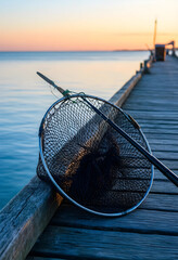 Fototapeta premium Fishing hobby and leisure activity, landing net and rod on wooden pier at sunset for outdoor recreation and travel lifestyle in coastal environment