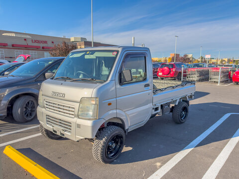Calgary, AB, Canada. Oct 2, 2026. A silver Suzuki Carry lifted kei truck parked in an outdoor retail parking lot on a sunny day.