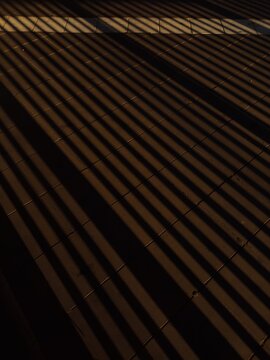 High-contrast abstract background featuring bold parallel lines of shadows cast across a stone tile ground during golden hour.