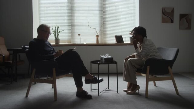 Middle aged Caucasian male psychologist counseling African American woman during therapy session. Clip fits mental health awareness campaigns and psychological counseling promotions