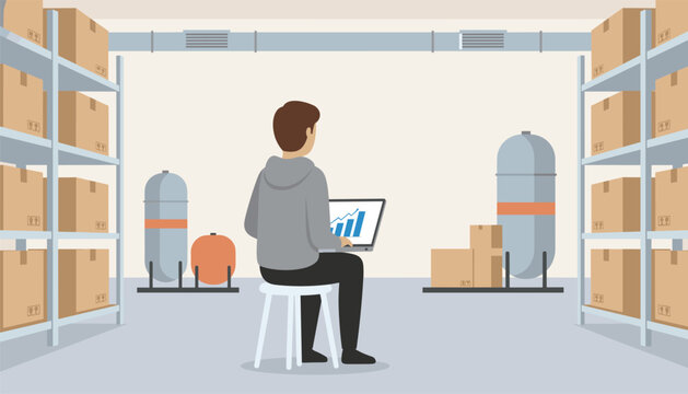 Warehouse worker sitting on a white stool while typing data analysis charts on a laptop computer inside storage facility.
