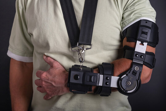 Man close up with a broken arm wearing in adjustable sling on black background