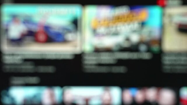 Defocused smart TV screen scrolling through a video streaming app interface with rows of video thumbnails. Abstract background for television, media and online entertainment.